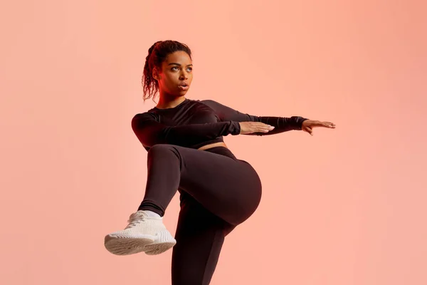 アフリカ系アメリカ人女性をスポーツウェアで暖め 足を持ち上げ 桃のネオンを背景に運動し スペースをコピーします エネルギーとスポーツ — ストック写真