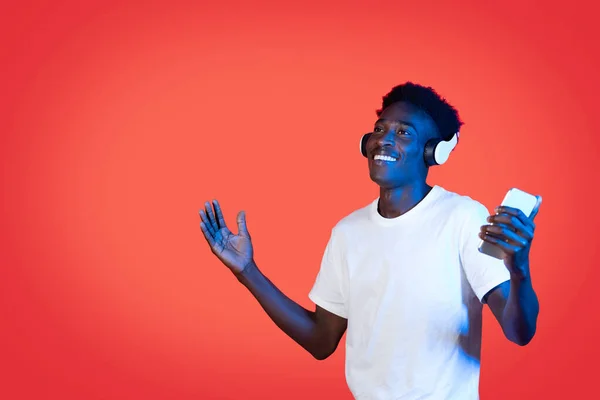 娱乐移动应用 在线内容概念 身穿白色T恤衫的快乐快乐的黑人小伙子拿着智能手机 用无线耳机 边跳舞边笑 望着复制的空间 — 图库照片
