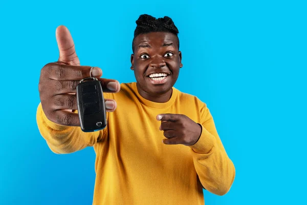 New Vehicle. Excited Black Man Pointing At Car Key In His Hand, Overjoyed Young African American Guy Celebrating Buying Own Auto, Standing Isolated Over Blue Studio Background, Copy Space