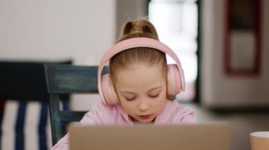 Güzel uzaktan öğrenme. Evinde internetten ders çalışan, dizüstü bilgisayar ve kulaklık takan, fotokopi kitaplarında görev yapan sevimli küçük kızın portresini kapat.