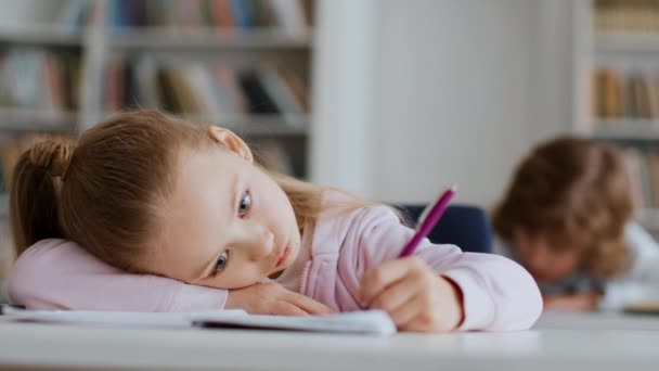 无聊的教育 紧贴躺在桌子上 在抄本上写作业 对学习不感兴趣 自由自在的小女孩的肖像 — 图库视频影像