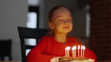 Doğum günü kutlaması. Sevimli küçük doğum günü kızının portresi. Dilek diliyor ve tatil pastasına mum üflüyor. Evde kameraya gülümsüyor.