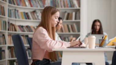 Kampüs kütüphanesinde. Üniversitede okuyan, proje yapan ya da testlere hazırlanan kız öğrencilerin çekimleri, kitaplar ve dizüstü bilgisayarla öğrenme, yavaş çekim, serbest alan