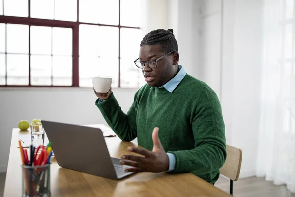 stock image Shocked Black Businessman Looking At Laptop Computer Holding Coffee Cup Having Issue With Online Work Sitting At Workplace In Modern Office. Business And Occupation Problems