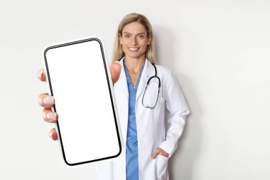 Gülen Doktor Üniformalı Kadın, hastanedeki Beyaz Duvar 'ın yanında dururken Büyük Boş Akıllı Telefon Ekranı' nı gösteriyor. Tıbbi Reklam İçin Kopya Alanı, Mockup