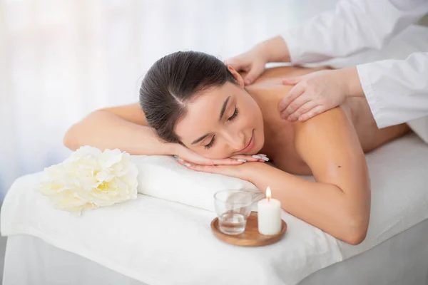Relaxing Massage. Beautiful Indian Female Enjoying Wellness Treatment In Spa Salon, Closeup Shot Of Professional Therapist Massaging Shoulders Of Young Hindu Female Lying On Table With Closed Eyes