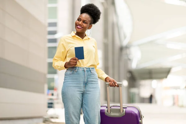 stock image Cheerful African American Female Tourist Holding Passport Standing Posing With Suitcase Near Airport Outside. Shot Of Happy Traveler Lady. Tourism And Cheap Flights Offer Concept