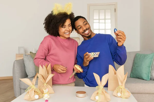 笑顔アフリカ系アメリカ人カップル開催イースターチョコレート卵自宅 幸せな若い黒人男性と女性選択フェスティバル御馳走と装飾手作りギフトバッグ 楽しむ休日のお祝い — ストック写真