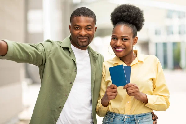Vacation Selfie. Cheerful Black Couple Posing Together Hugging And Showing Passports To Camera Standing Outside Near Airport Terminal. Shot Of Happy Tourists. Family Travel Concept