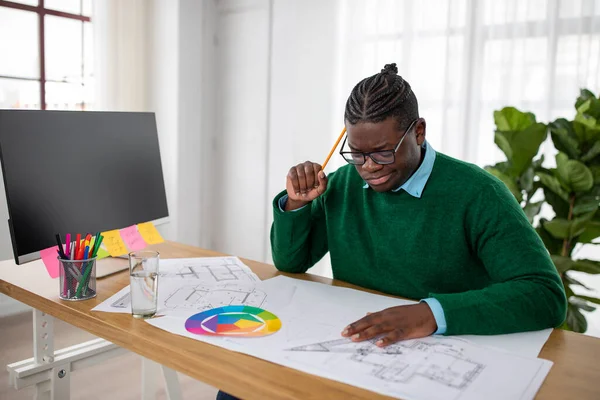 Pensive Black Engineer Man Making Technical Drawing Of An Object Thinking And Solving Problems Sitting At Desk In Modern Office. Architecture And Engineering Design Career Concept
