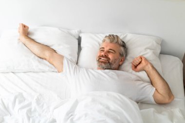 Mutlu gülümseyen orta yaşlı, yatakta tek başına yatan, uyandıktan sonra kollarını açan, dinlenmiş hisseden, yeni güne hazır, fotokopi odasına bakan, yukarıdan bakan,