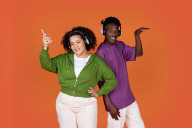 Neşeli, mutlu, çoklu etnik çeşitlilikte genç bir çift Afro-Amerikan erkeği ve İspanyol bayan kırmızı arka planda müzik dinleyip dans ediyorlar, akıllı telefon ve kablosuz kulaklık kullanıyorlar.