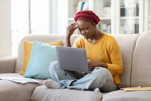 疲れているカジュアルな赤いアフリカのターバンソファに座って着て 自宅でコンピュータを使用して 頭に触れ オンラインで作業し 疲れを感じ コピースペース若い黒人女性動揺 仕事の書き込みの概念 — ストック写真