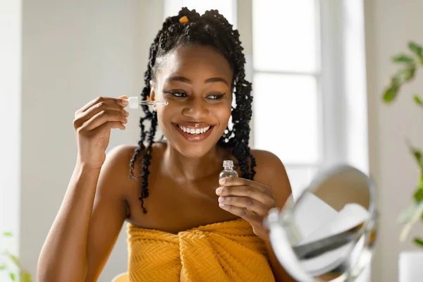 Hermosa Dama Negra Aplicando Suero Facial Sonriendo Espejo Sentada Envuelta —  Fotos de Stock