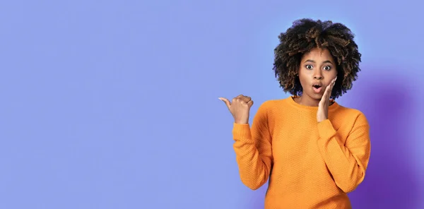 ショックを受けた若いですアフリカ系アメリカ人女性でオレンジでブッシーな髪を指していますコピースペースとタッチ彼女の顔以上紫のスタジオ背景 バナー付きモックアップ広告 — ストック写真