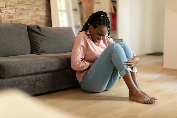 Młoda Afroamerykanka Cierpiąca Ból Brzucha Siedząca Podłodze Przy Kanapie Dotykająca — Zdjęcie stockowe