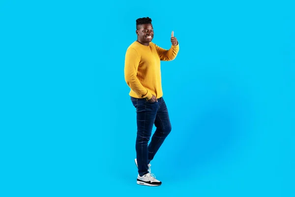Yakışıklı Genç Siyah Adam Stüdyoda Mavi Arkaplan Üzerinde Dikilirken Başparmağını — Stok fotoğraf