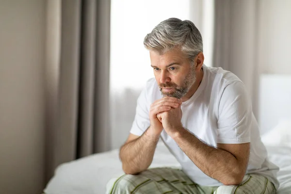 闷闷不乐的中年白发苍苍的英俊男人穿着睡衣 独自坐在床上 患有忧郁症 孤独或焦虑 复制着空间 中年危机 — 图库照片