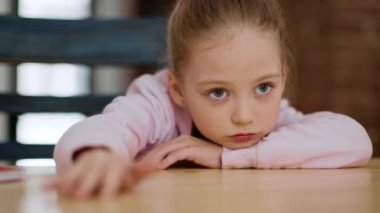 Sıkıcı ruh hali. Sevimli üzgün küçük kızın portresi. Sıkılmış ve kayıtsız. Masaya uzanmış, parmaklarıyla hafifçe vuruyor.