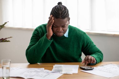 Finansal sorunlar. Mutsuz Afro-Amerikan Adam, Modern Ofiste Masada Oturan Hesap Makinesini kullanarak Masrafları ve Faturaları Hesaplıyor. Kriz ve İş Muhasebe Sorunları Kavramı