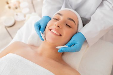 Uzman kozmetik uzmanı, güzellik salonunda yüz bakımı sırasında pamuklu ped kullanan Hintli genç bir kadının derisini temizliyor. Güzellik salonunda rahatlamış Hindu bir kadının sağIık gününün tadını çıkartıyor.