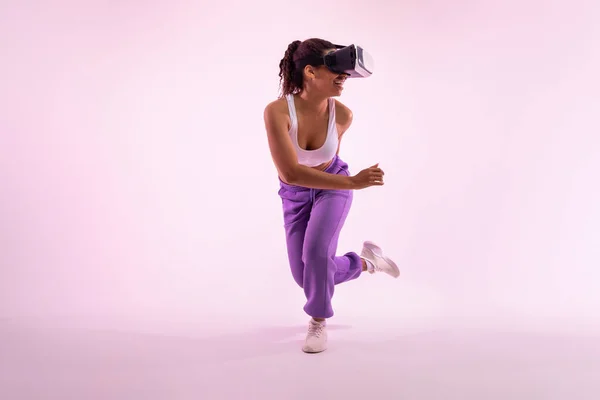 stock image Joyful black woman enjoying virtual reality experience in modern vr headset, fit young lady enjoying 3D fitness class over pink neon light background, copy space