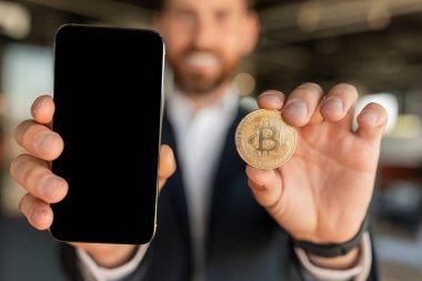 Kripto para birimi uygulaması. Altın Bitcoin ve boş akıllı telefon ekranı gösteren bir işadamı, çevrimiçi ticaret uygulaması öneriyor, model, seçici odaklanma