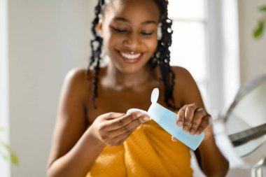 Mutlu siyah kadın pamuk altlığa mikiler suyu dolduruyor, yatak odasının içinde oturuyor, seçici odaklanma, boş alan. Günlük derin temizlik kavramı