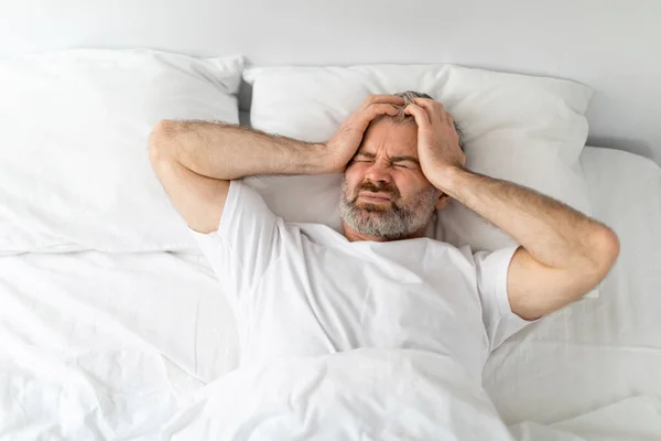 家で目を閉じてベッドに横たわっている不幸な病気の中年男 頭に触れる 朝の頭痛で疲れた男性の目覚め 慢性片頭痛に苦しんで 上のビュー コピースペース — ストック写真