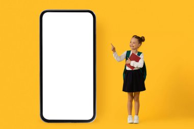 Boş beyaz ekranlı büyük akıllı telefonu işaret eden sevimli küçük liseli kız, ders kitabı tutan kız çocuğu ve eğitim uygulaması ya da web sitesi için kopya alanı gösteren kolaj,