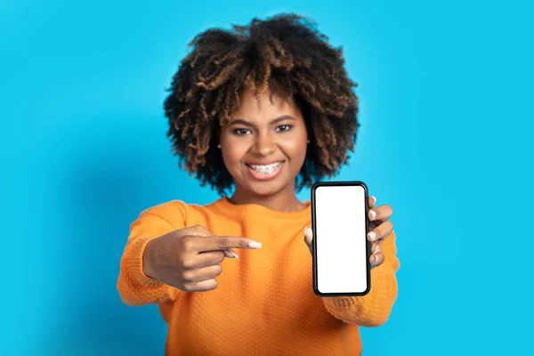 现代智能手机 黑色女人手中拿着白色的空屏幕 一位快乐迷人的非洲女士指着手机 带着模仿的空广告空间 蓝色背景 — 图库照片