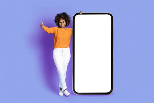 快乐快乐的年轻黑人女人 浓密的头发 拿着大手机 白色的空屏幕 在紫色工作室的背景上露出大拇指 推荐漂亮的应用程序 — 图库照片