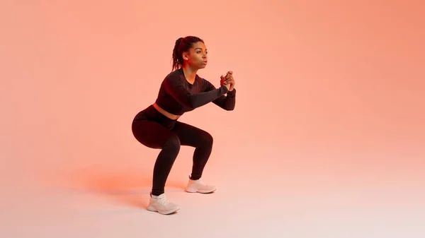 トレーニングコンセプト 桃のネオンスタジオの背景 無料のスペースのパノラマ上で動作し スクワット演習を行うアフリカ系アメリカ人女性に合わせてください 健康的なライフスタイル — ストック写真