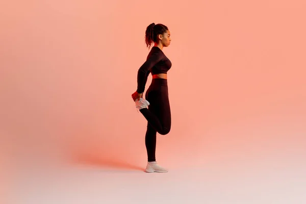 スポーツウェアの黒の女性は 桃のネオンスタジオの背景に足の筋肉を伸ばし フル長さ コピースペースを暖める フィットネスワークアウトを持つアスレチック女性 — ストック写真
