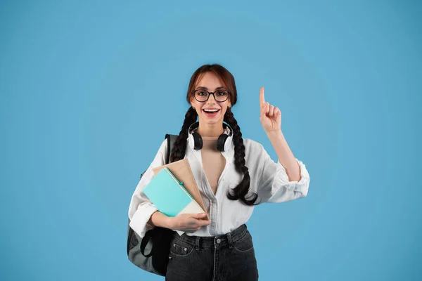 令人高兴的是 受到启发的欧洲少女学生带着辫子 带着背包的眼镜 书显示了蓝色工作室背景下的空旷空间 有主意 解决学习和教育问题 — 图库照片