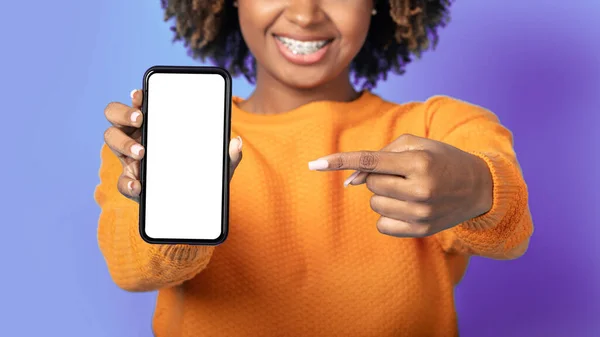 Cell phone with white empty screen in female hands, cropped of black lady pointing at smartphone with blank display, recommending nice mobile app or offer, mockup, purple background