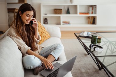 Akıllı telefondan arayan, içerideki bilgisayarda yazan mutlu Asyalı kadın. İletişim uzaktan kumandası, iş, evdeki iş, teknoloji ve sosyal ağlarla yeni normal