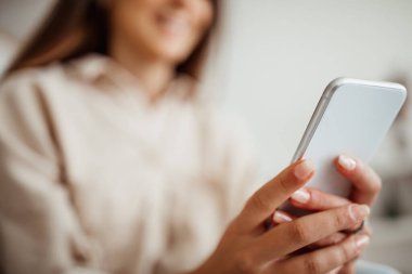 Akıllı telefondan yazı yazan, sosyal ağda sohbet eden, video izleyen, iç mekanda internette sörf yapan gülümseyen Asyalı genç bir kadın. Kapatın. Uygulama, web sitesi ve blog evde