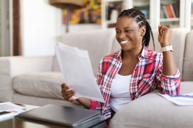 Duygusal, genç, çekici siyahi bir bayan, günlük kıyafetli girişimci, elinde dizüstü bilgisayarla çay masasında oturuyor, gazete okuyor ve el kol hareketi yapıyor, başarıyı kutluyor, evden çalışıyor, uzayı kopyalıyor.