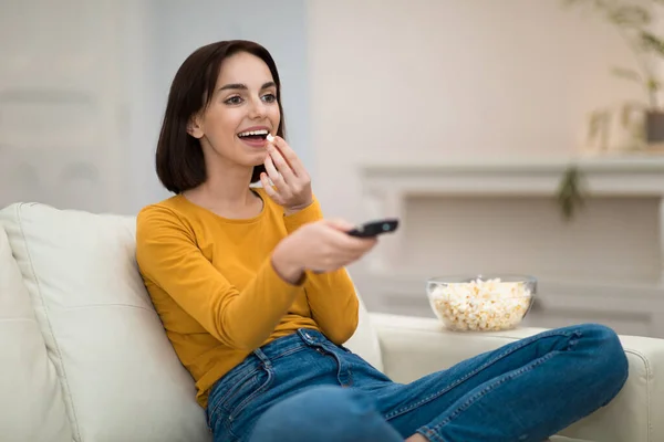 一个人坐在沙发上 手握遥控器 吃爆米花 周末在家里放松 看电视 复制空间 快乐而美丽的黑发女子 — 图库照片