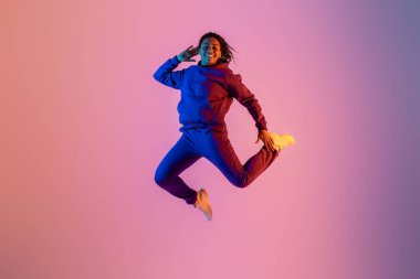 Neşeli, enerjik siyahi kadın spor giyim sektöründe neon renkli stüdyo arka planı, tam boy, boş alan, afiş ile eğleniyor ve yükseliyor.