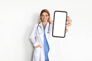 Beyaz önlüklü, elinde büyük ekranlı akıllı telefonu olan güzel doktor kadın üniformalı gülümseyen terapist tıbbi reklamlar için kopyalama alanı sunuyor.