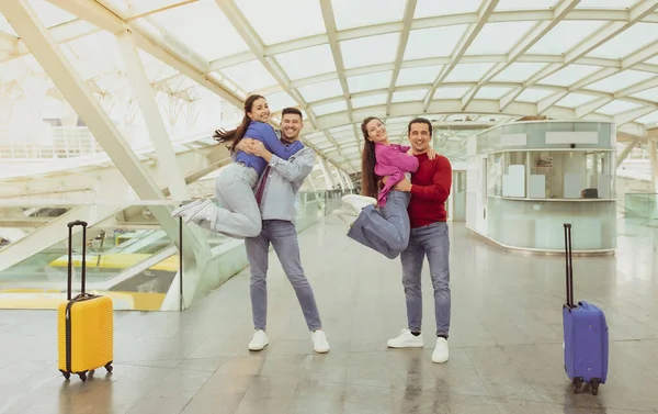 Travel With Friends. Two Joyful Couples Celebrating Vacation Posing Together And Having Fun In Modern Airport Terminal Indoors. Cheap Tours And Tickets Offer Concept. Full Length Shot