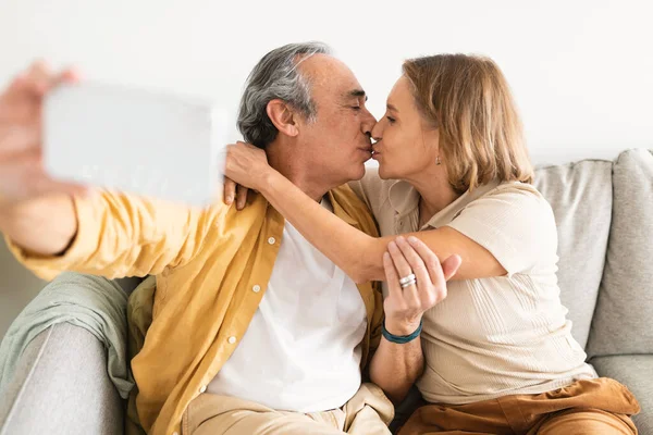 Milující Starší Manželé Berou Selfie Mobil Líbání Sedí Objímají Doma — Stock fotografie