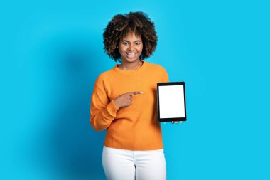 Siyah kadının elinde beyaz beyaz ekranlı dijital cihaz, neşeli Afrikalı Amerikalı kadın tableti işaret ediyor reklam için boş bir yer, mavi arkaplan
