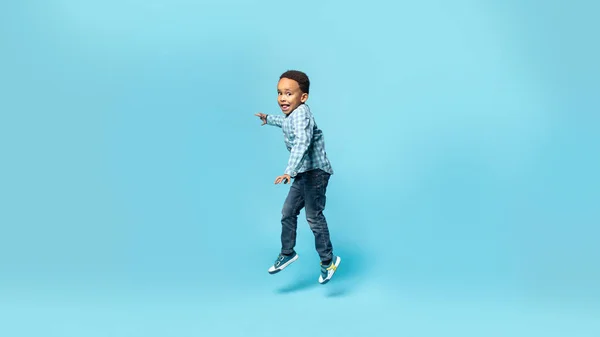 可笑的非洲裔美国小男孩在空中跳跃 在蓝色的工作室背景上鬼混 全身而退 全景尽收眼底 积极的男孩玩乐 — 图库照片