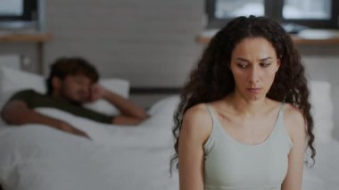 İlişki krizi. Depresyondaki orta doğulu genç bir kadının yatakta oturup mutsuz aile hayatını düşünürken, kocasının yatakta, yavaş çekimde, boş alanda uyuduğunu yakından çek.