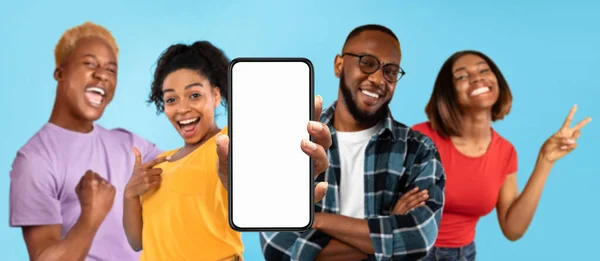 Cheerful excited millennial african american people point finger at smartphone with blank screen, enjoy win isolated on blue studio background, panorama. Great website, app, ad and offer