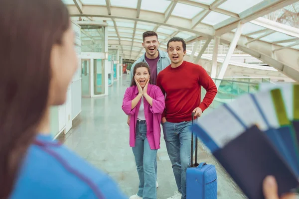 旅行の申し込み 現代の空港の屋内でスーツケースと一緒に休暇中に旅行する彼女の興奮した友人に搭乗券を示す女性 格安航空券を提供する女性 選択的フォーカス — ストック写真