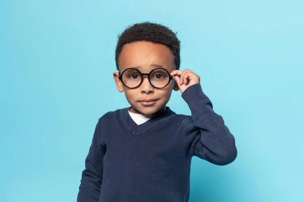 聪明的非洲裔美国小男孩 身穿校服 触摸眼镜 看着相机 站在蓝色的工作室背景下 自由自在 — 图库照片